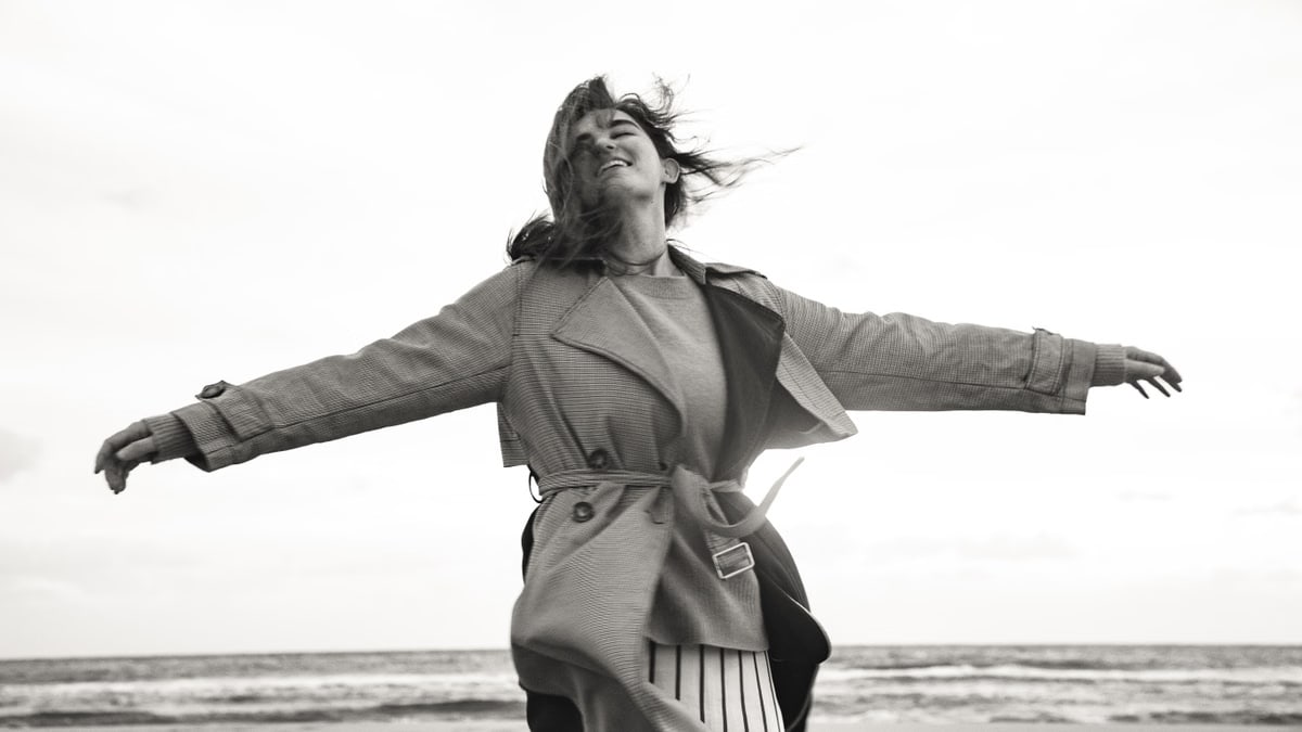Woman in a coat feeling free on a windy beach day in black and white photography.
