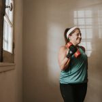A woman lifting dumbbells indoors by a window, focused on her workout routine.